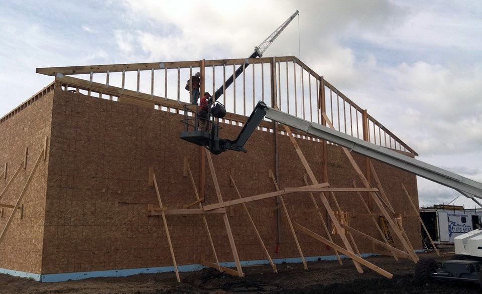 Commercial construction workers framing a large building using heavy equipment.