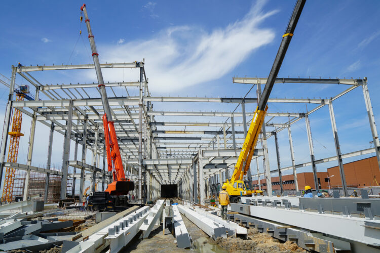 Workers assembling a pre-engineered steel structure with cranes