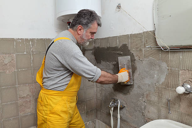 Bathroom remodeling contractor applying plaster to tiled wall