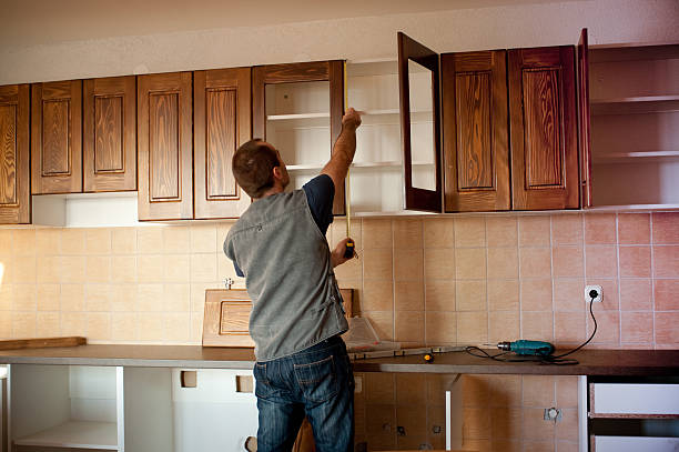 Worker measuring upper wooden kitchen cabinets during installation