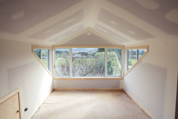 Attic bedroom conversion in progress, featuring large windows and drywall